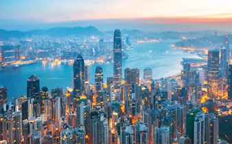 Aerial view of Hong Kong Island skyline at dusk with illuminated skyscrapers and Victoria Harbour.
