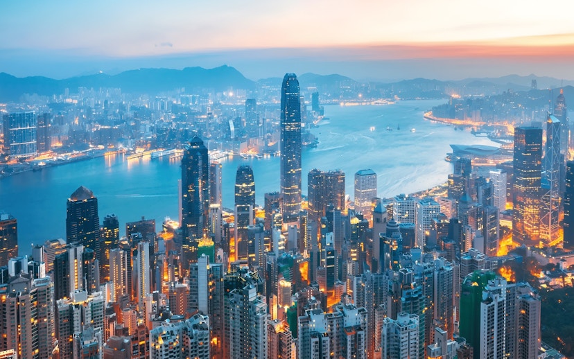 Aerial view of Hong Kong Island skyline at dusk with illuminated skyscrapers and Victoria Harbour.
