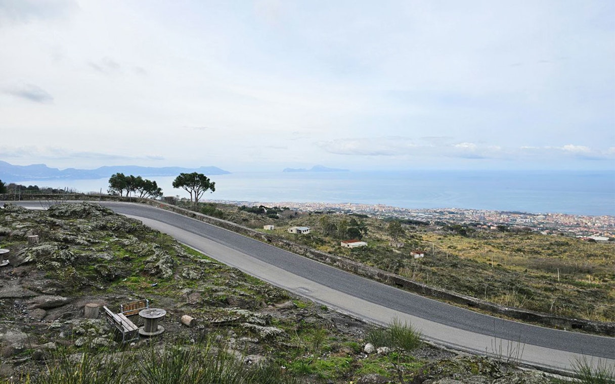 Winding road on Mount Vesuvius with view of Sorrento coastline and sea.