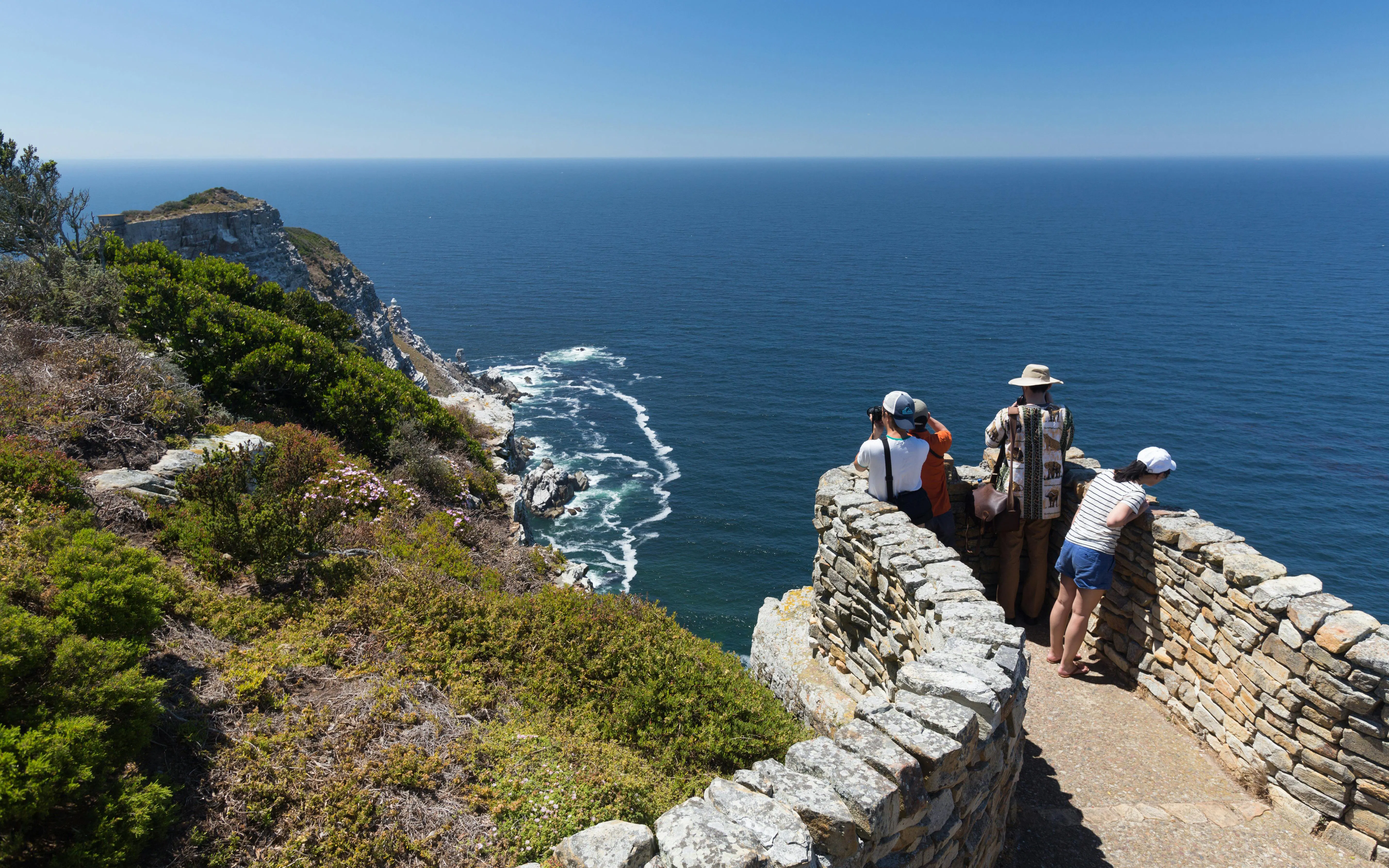 Visitors observing ocean views from a stone lookout at Cape Point, South Africa.