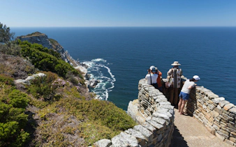 Visitors observing ocean views from a stone lookout at Cape Point, South Africa.