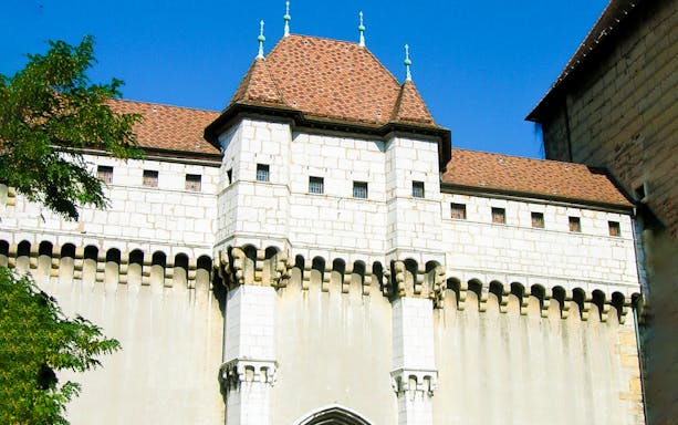 Medieval castle facade in Annecy, France, with stone walls and red-tiled roof.