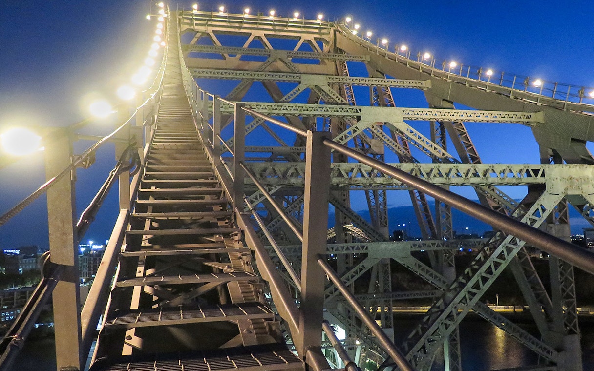 Climbing stairs on Brisbane Story Bridge at twilight.