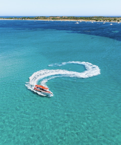 Red boat making a 360-degree turn, creating a white wake in turquoise water.