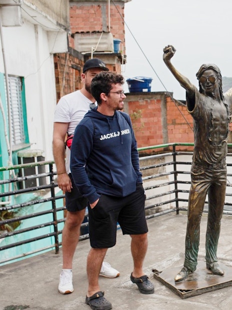 Tourists with guide at a viewpoint in Santa Marta, Rio, near a statue overlooking the city.