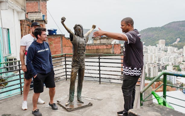 Tourists with guide at a viewpoint in Santa Marta, Rio, near a statue overlooking the city.