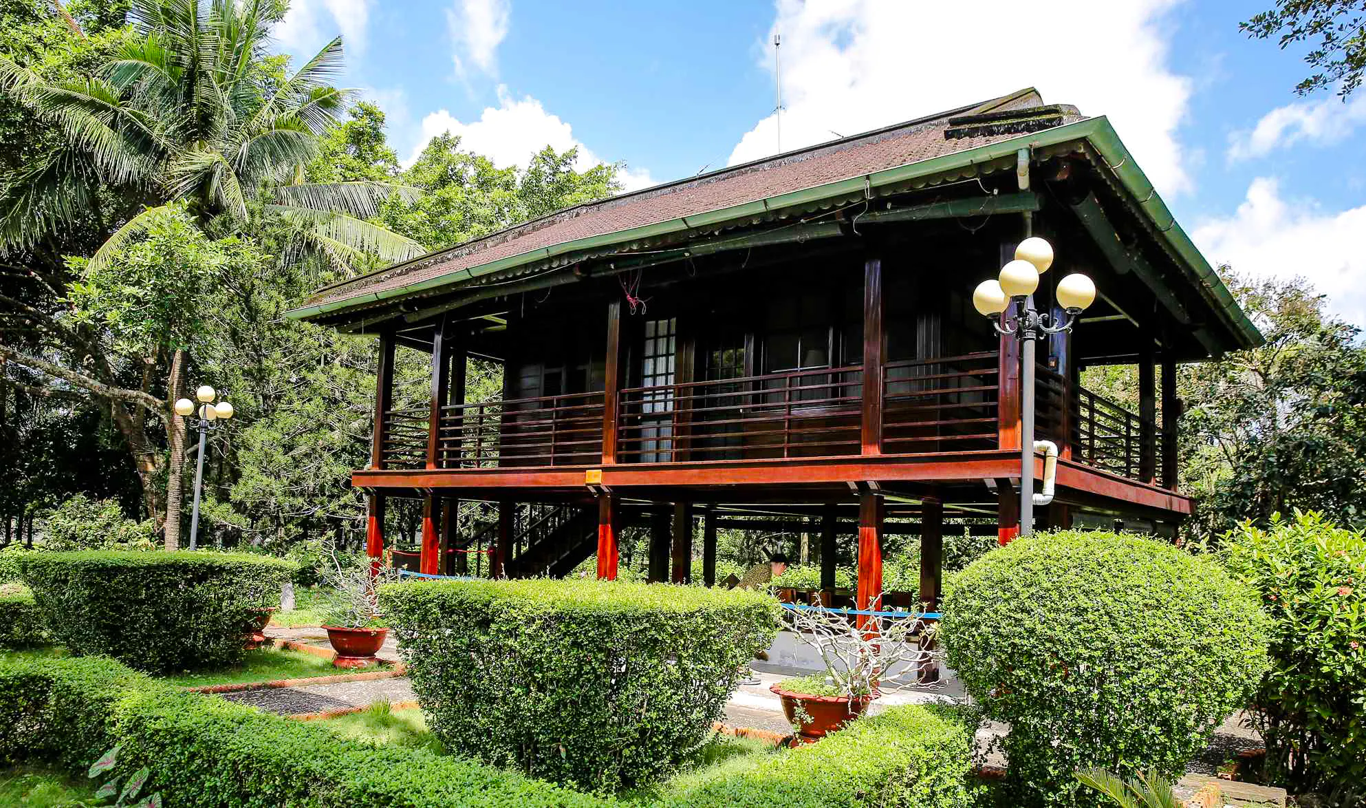 Traditional stilt house in Ho Chi Minh Mausoleum complex, Hanoi, surrounded by lush greenery.