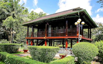 Traditional stilt house in Ho Chi Minh Mausoleum complex, Hanoi, surrounded by lush greenery.