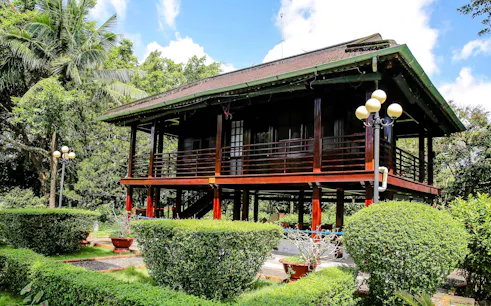 Traditional stilt house in Ho Chi Minh Mausoleum complex, Hanoi, surrounded by lush greenery.