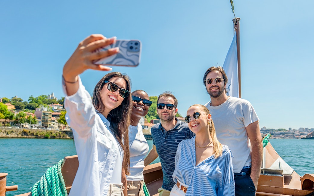Tourists taking selfies on a Douro River cruise with scenic views of Porto.