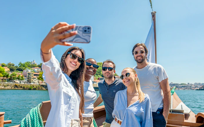 Tourists taking selfies on a Douro River cruise with scenic views of Porto.