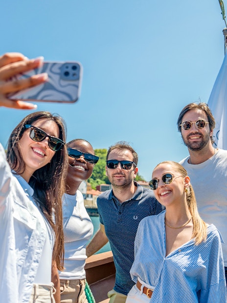 Tourists taking selfies on a Douro River cruise with scenic views of Porto.