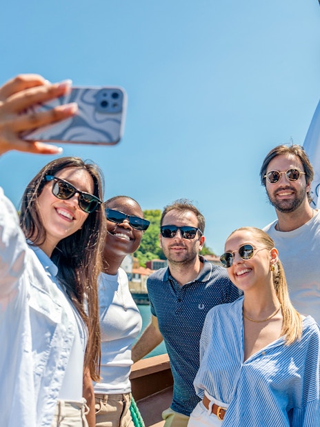Tourists taking selfies on a Douro River cruise with scenic views of Porto.