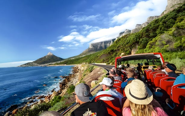 Open-top bus tour along ocean road with view of Lion's Head and Table Mountain, Cape Town.