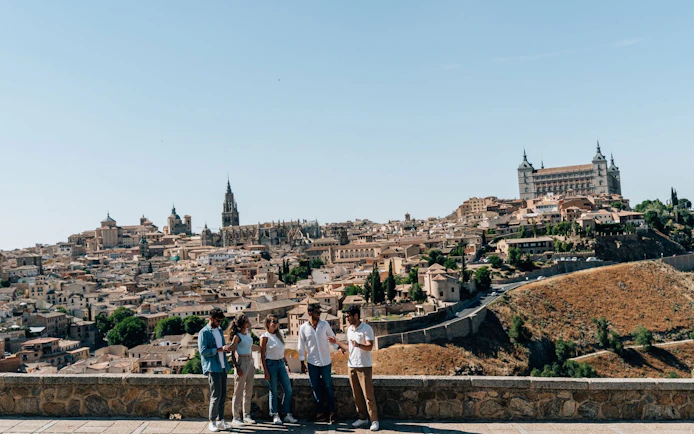 Tourists with guide overlooking Toledo cityscape from a viewing point.