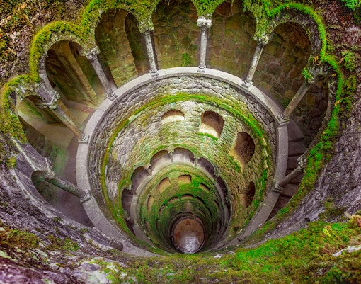 Initiation well at Quinta da Regaleira, Sintra, with spiral staircase and lush greenery.