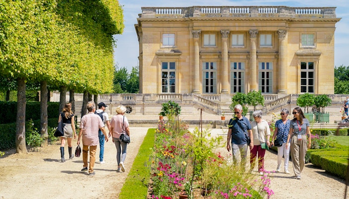 Tourist with guide at Petit Trianon exploring garden and flowers in Versailles, France.
