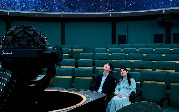 Young couple seated at Konica Minolta Planetaria TOKYO Ginza, gazing at starry dome.