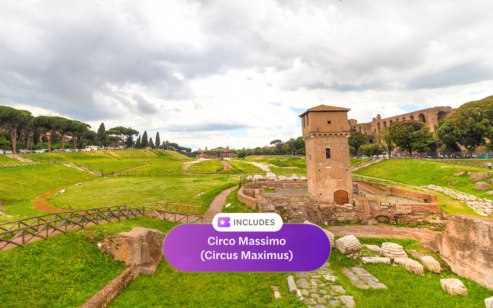 Ancient ruins and tower at Circo Massimo, Rome, with green landscape and cloudy sky.