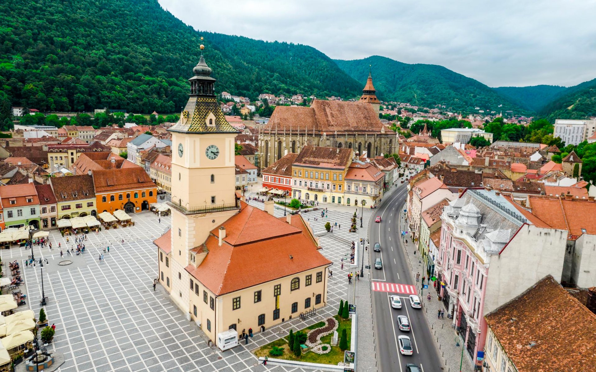 Council Square and Black Church in Brasov city center, Romania, with surrounding buildings and mountains.