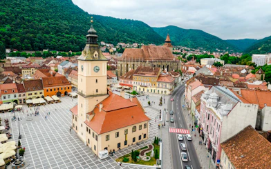 Council Square and Black Church in Brasov city center, Romania, with surrounding buildings and mountains.