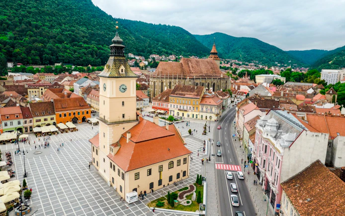 Council Square and Black Church in Brasov city center, Romania, with surrounding buildings and mountains.