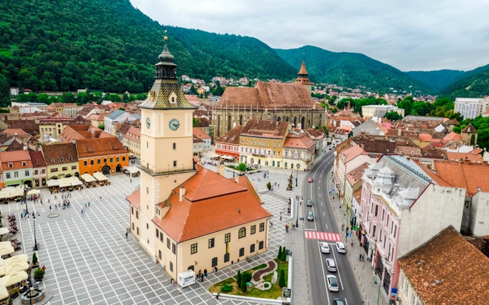 Council Square and Black Church in Brasov city center, Romania, with surrounding buildings and mountains.