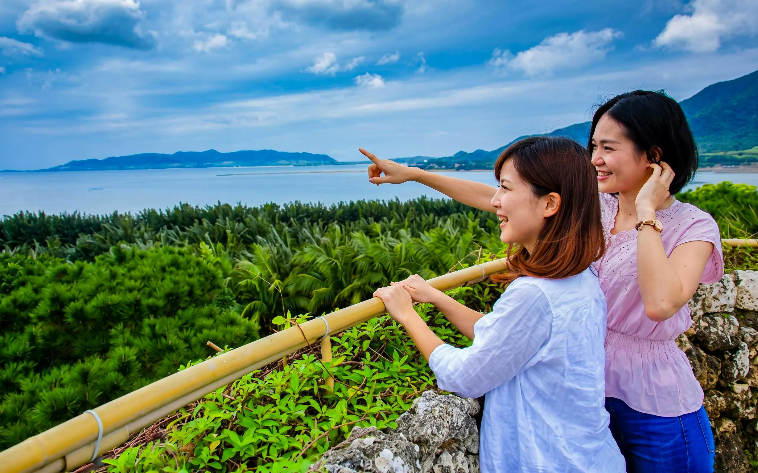 Visitors enjoying the view at Ishigaki Yaima Village, overlooking lush greenery and the ocean.