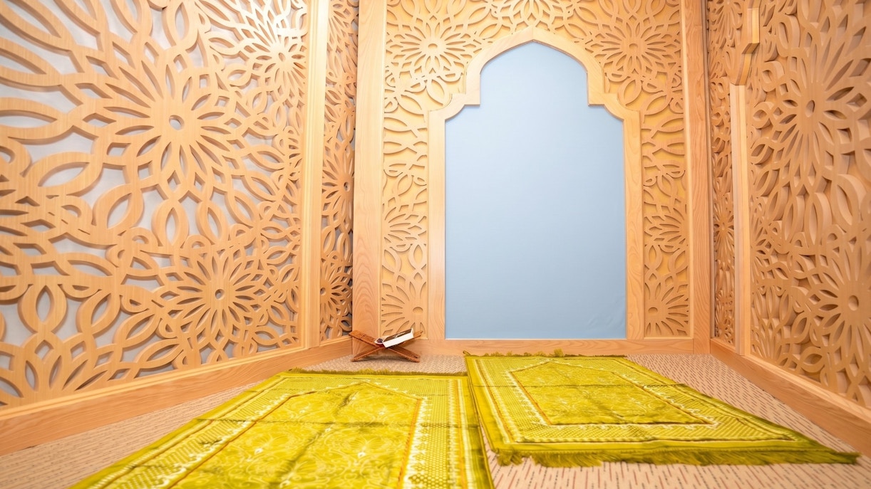 Prayer room with intricate wooden lattice design and green prayer mats at Jasmine Halal Lounge, Tan Son Nhat Airport.