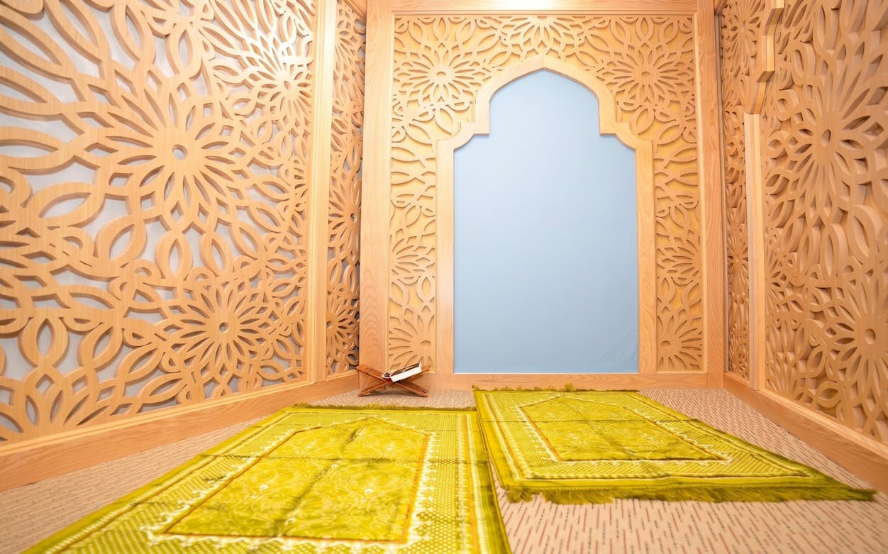Prayer room with intricate wooden lattice design and green prayer mats at Jasmine Halal Lounge, Tan Son Nhat Airport.