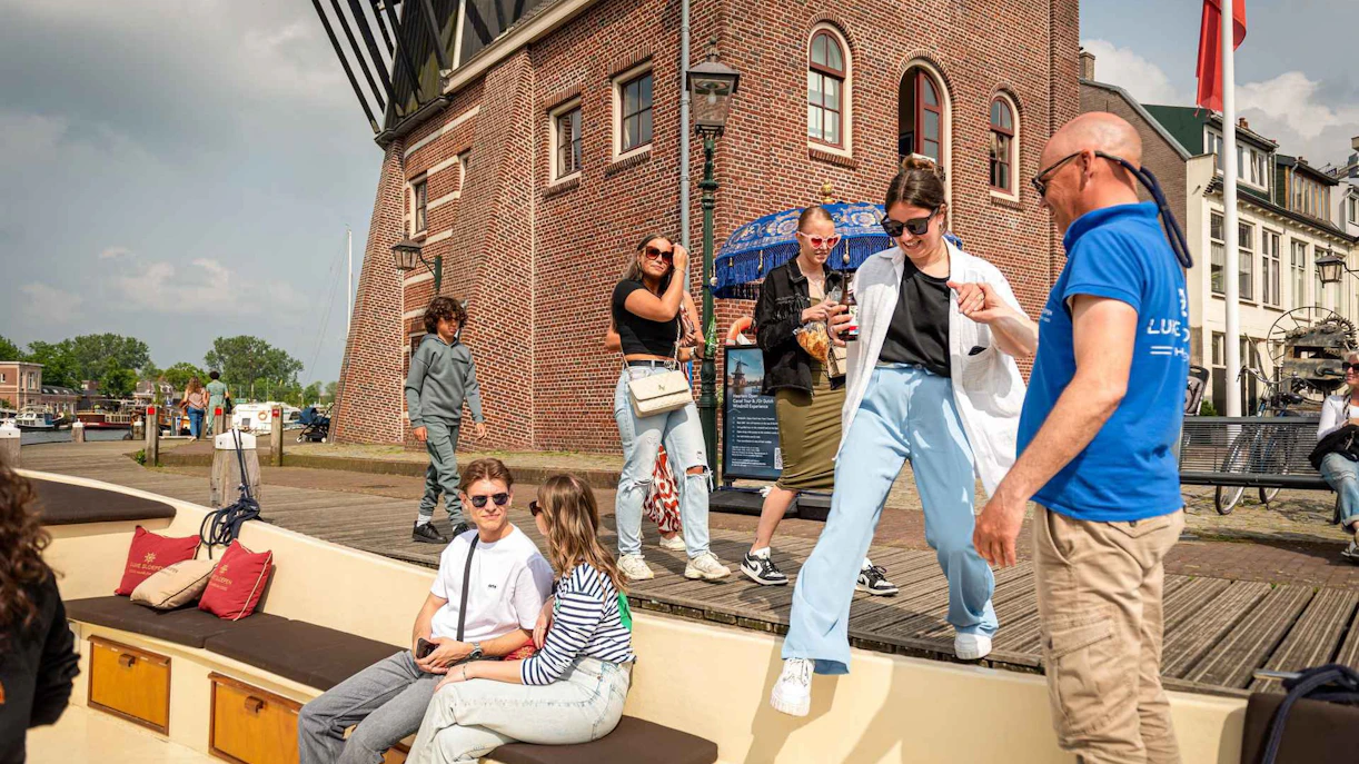 People boarding an open boat for a Harlem canal cruise near a historic brick building.