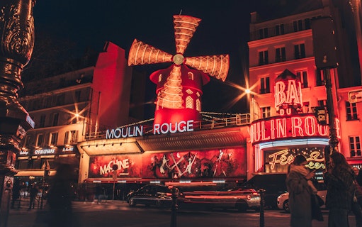 Moulin Rouge illuminated at night in Paris, featuring iconic red windmill and vibrant neon lights.