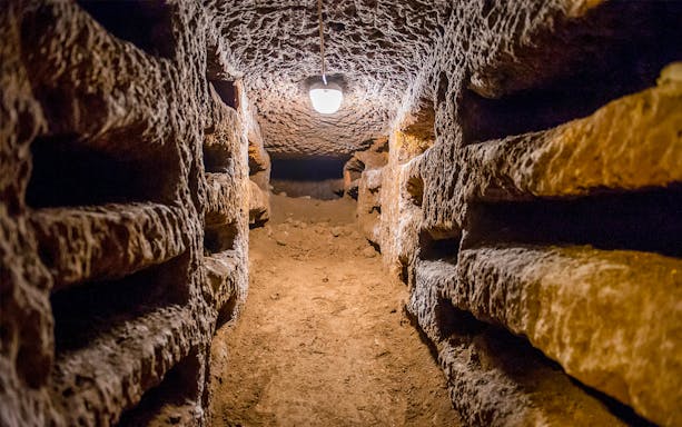 Underground passage in the Catacombs of Rome with stone walls and dim lighting.