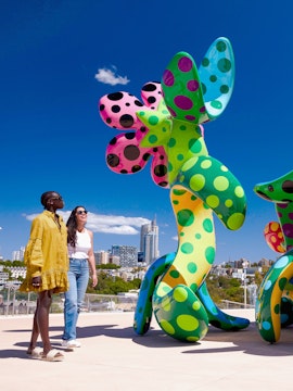 Women viewing Yayoi Kusama's "Flowers that Bloom in the Cosmos" sculpture in a cityscape setting.