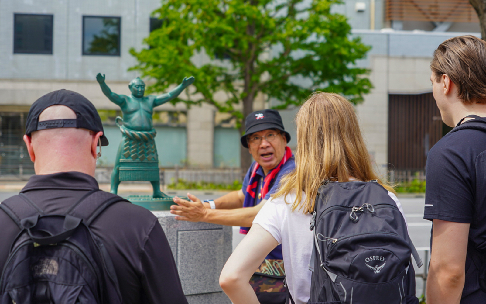 Tourists listening to a guide near a sumo statue in Ryogoku.