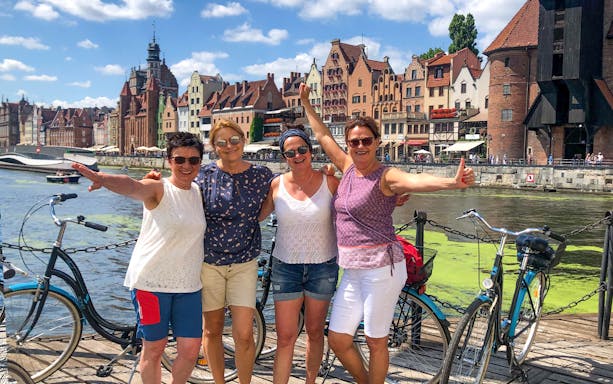 Group of tourists enjoying a bike tour along the Motława River in Gdansk, with historic buildings in the background.