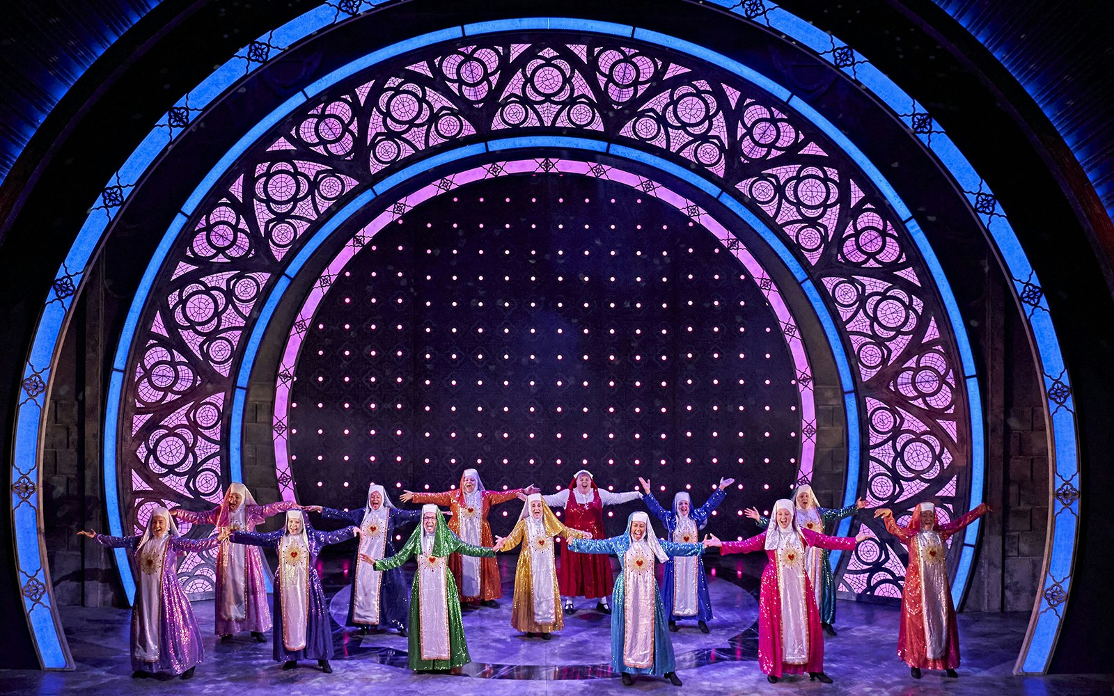 Performers in colorful habits on stage during a "Sister Act" musical scene.