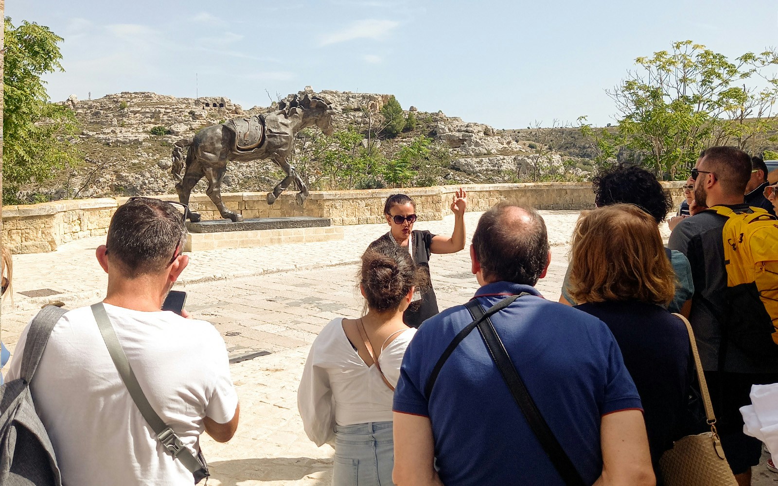 Tour group in Matera listening to a guide near a horse statue, with rocky landscape in the background.