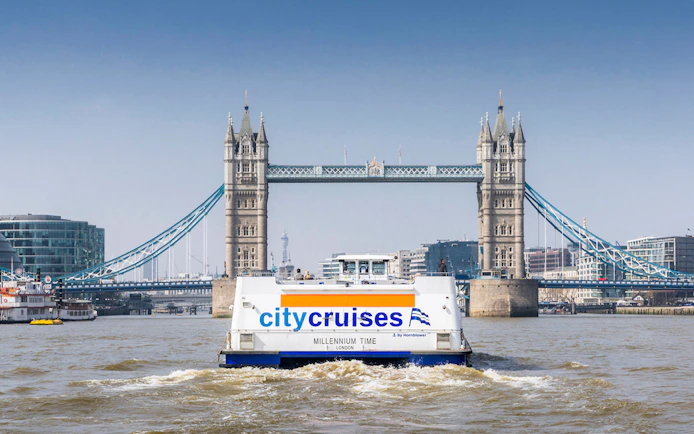 City cruise boat on Thames River with Tower Bridge in the background, London.