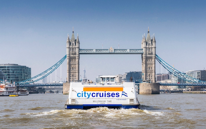 City cruise boat on Thames River with Tower Bridge in the background, London.