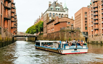 Harbor cruise boat in Hamburg's Speicherstadt canal with historic brick warehouses.
