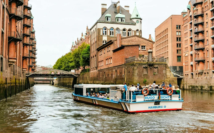 Harbor cruise boat in Hamburg's Speicherstadt canal with historic brick warehouses.