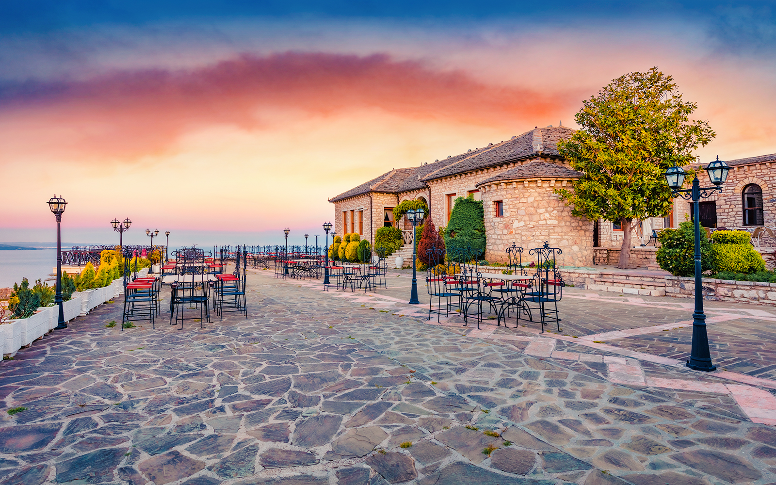 Lekursi Castle terrace with empty tables at sunset, overlooking the sea.
