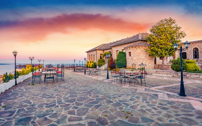 Lekursi Castle terrace with empty tables at sunset, overlooking the sea.