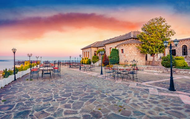 Lekursi Castle terrace with empty tables at sunset, overlooking the sea.