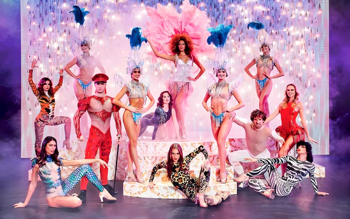 Paradis Latin show performers in vibrant costumes on stage with dinner setting.
