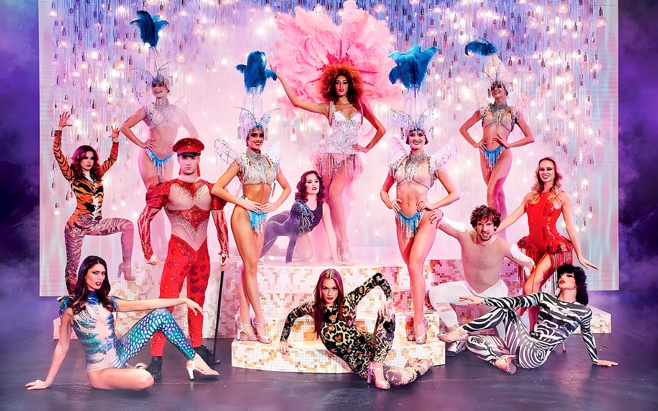 Paradis Latin show performers in vibrant costumes on stage with dinner setting.