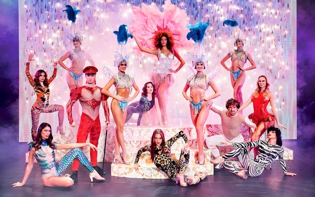 Paradis Latin show performers in vibrant costumes on stage with dinner setting.