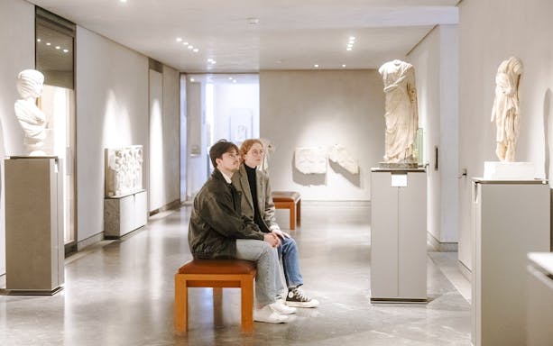 Visitors seated in the Museum of Fine Arts, Lyon, France, observing classical sculptures.