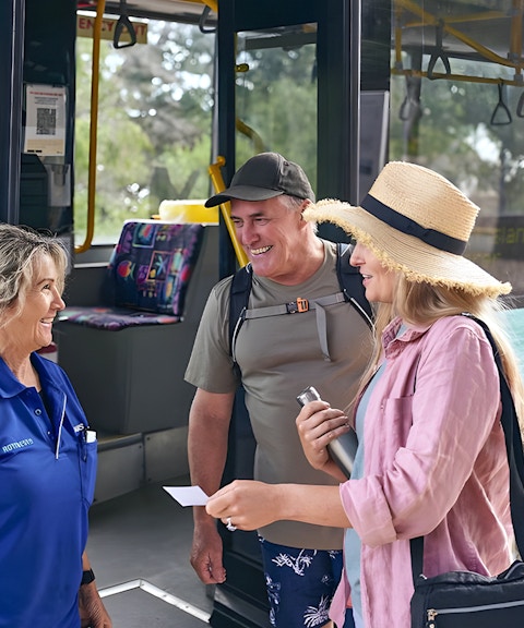 Tourists boarding a bus, assisted by a staff member, with luggage in the background.